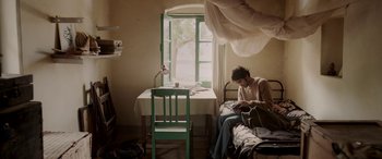 Movie still from “A Death in the Gunj” (2016), directed by Konkona Sen Sharma – A woman sitting at a table in front of an open window; Wide shot, Low angle