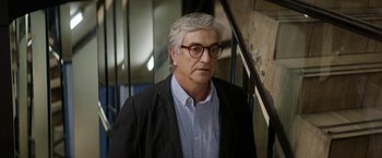 Movie still from “A Fantastic Woman” (2017), directed by Sebastián Lelio – An older man wearing glasses standing next to a staircase; Close Up shot, Over the shoulder angle