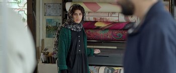 Movie still from “A Hero” (2021), directed by Asghar Farhadi – A woman standing in front of a pile of fabrics; Medium shot, Over the shoulder angle