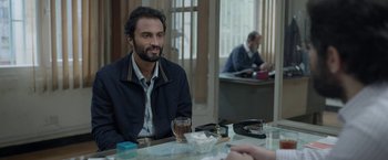 Movie still from “A Hero” (2021), directed by Asghar Farhadi – A man sitting at a table with a drink in front of him; Medium shot, Over the shoulder angle