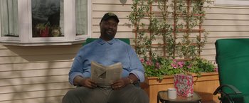 Movie still from “A Journal for Jordan” (2021), directed by Denzel Washington – A man sitting in a chair reading a newspaper; Medium shot, Over the shoulder angle
