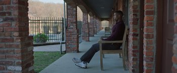 Movie still from “A Journal for Jordan” (2021), directed by Denzel Washington – A man sitting on top of a wooden bench on a porch; Wide shot, Over the shoulder angle