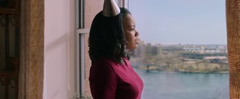 Movie still from “A Journal for Jordan” (2021), directed by Denzel Washington – A woman wearing a party hat standing in front of a window; Medium shot, Over the shoulder angle