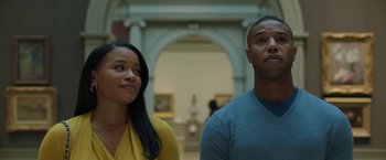 Movie still from “A Journal for Jordan” (2021), directed by Denzel Washington – A man and a woman standing in front of a painting; Medium shot, Low angle