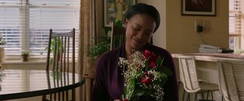 Movie still from “A Journal for Jordan” (2021), directed by Denzel Washington – A woman sitting in a chair holding a bouquet of flowers; Medium shot, Over the shoulder angle