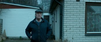 Movie still from “A Man Called Ove” (2015), directed by Hannes Holm – An older man standing in front of a brick building; Medium shot, Low angle