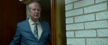 Movie still from “A Man Called Ove” (2015), directed by Hannes Holm – An older man wearing a suit and tie standing in front of a door; Medium shot, Over the shoulder angle