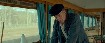 Movie still from “A Man Called Ove” (2015), directed by Hannes Holm – A man wearing a black hat sitting in front of a window; Medium shot, Low angle