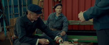 Movie still from “A Man Called Ove” (2015), directed by Hannes Holm – Two men sitting on the ground eating and drinking; Medium shot, Over the shoulder angle
