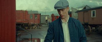 Movie still from “A Man Called Ove” (2015), directed by Hannes Holm – A young man in a blue jacket and a gray hat; Medium shot, Low angle