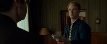 Movie still from “A Man Called Ove” (2015), directed by Hannes Holm – A man holding a newspaper while standing next to a lamp; Medium shot, Over the shoulder angle