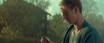 Movie still from “A Man Called Ove” (2015), directed by Hannes Holm – A man looking at his cell phone while standing in front of trees; Close Up shot, Low angle