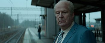 Movie still from “A Man Called Ove” (2015), directed by Hannes Holm – An older man wearing a suit and tie standing in front of a train station; Close Up shot, Over the shoulder angle