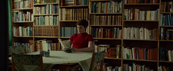 Movie still from “A Man Called Ove” (2015), directed by Hannes Holm – A woman sitting at a table reading a book in front of a bookcase; Medium shot, Low angle