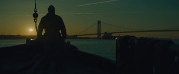 Movie still from “A Most Violent Year” (2014), directed by J.C. Chandor – A man standing on the side of a boat in front of a bridge; Extreme Wide shot, Low angle