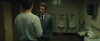 Movie still from “A Most Violent Year” (2014), directed by J.C. Chandor – A man in a gray suit and red tie standing in front of a urinal; Medium shot, Over the shoulder angle