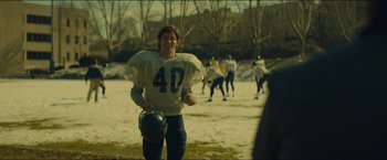 Movie still from “A Most Violent Year” (2014), directed by J.C. Chandor – A man holding a helmet while standing on a field; Medium shot, Over the shoulder angle