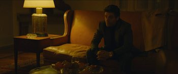 Movie still from “A Most Violent Year” (2014), directed by J.C. Chandor – A man sitting on top of a leather couch next to fruit; Medium shot, Over the shoulder angle