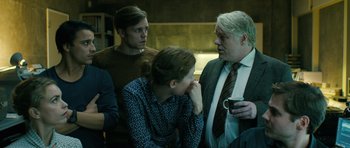 Movie still from “A Most Wanted Man” (2014), directed by Anton Corbijn – A group of people standing next to each other in a room; Medium shot, Over the shoulder angle