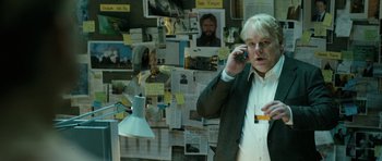 Movie still from “A Most Wanted Man” (2014), directed by Anton Corbijn – A man talking on a cell phone in front of a bulletin board; Medium shot, Over the shoulder angle