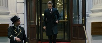 Movie still from “A Most Wanted Man” (2014), directed by Anton Corbijn – A man in a suit and tie standing in front of a door way; Wide shot, Low angle