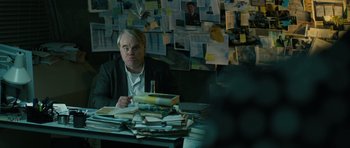 Movie still from “A Most Wanted Man” (2014), directed by Anton Corbijn – A man sitting at a table with a stack of books on top of it; Medium shot, Over the shoulder angle