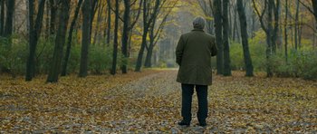 Movie still from “A Most Wanted Man” (2014), directed by Anton Corbijn – An older man is standing on a path in the woods; Wide shot, Over the shoulder angle
