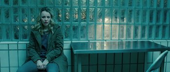 Movie still from “A Most Wanted Man” (2014), directed by Anton Corbijn – A woman sitting on top of a bench in front of a glass block wall; Medium shot, Over the shoulder angle