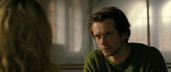 Movie still from “A Most Wanted Man” (2014), directed by Anton Corbijn – A man in a green sweater stares at the camera; Close Up shot, Over the shoulder angle