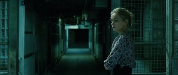 Movie still from “A Most Wanted Man” (2014), directed by Anton Corbijn – A woman standing in a dark hallway looking at the camera; Medium shot, Over the shoulder angle