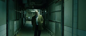Movie still from “A Most Wanted Man” (2014), directed by Anton Corbijn – An older man wearing a green coat and a tie; Medium shot, Over the shoulder angle