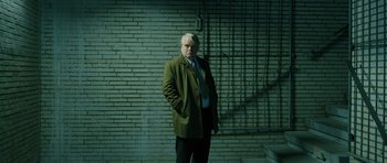 Movie still from “A Most Wanted Man” (2014), directed by Anton Corbijn – A man in a suit and tie standing in front of a brick wall; Medium shot, Low angle