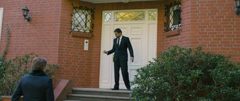 Movie still from “A Most Wanted Man” (2014), directed by Anton Corbijn – A man wearing a suit and tie standing in front of a door; Wide shot, Low angle