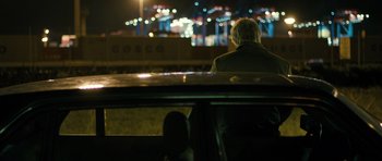 Movie still from “A Most Wanted Man” (2014), directed by Anton Corbijn – A man sitting in the back of a car at night; Wide shot, Over the shoulder angle