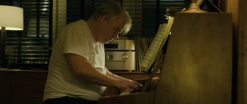 Movie still from “A Most Wanted Man” (2014), directed by Anton Corbijn – An older man is playing the piano in a recording studio; Medium shot, Low angle