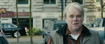 Movie still from “A Most Wanted Man” (2014), directed by Anton Corbijn – A person wearing a jacket near a building; Close Up shot, Over the shoulder angle
