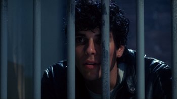 Movie still from “A Nightmare on Elm Street” (1984), directed by Wes Craven – A young man with curly hair is looking through a fence; Close Up shot, Low angle