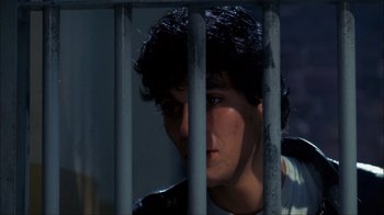 Movie still from “A Nightmare on Elm Street” (1984), directed by Wes Craven – A young man behind a metal fence looking at the camera; Close Up shot, Low angle