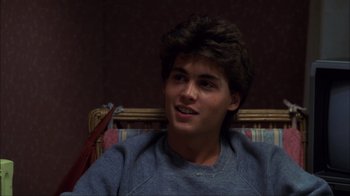 Movie still from “A Nightmare on Elm Street” (1984), directed by Wes Craven – A young man sitting in a chair smiling for the camera; Close Up shot, Over the shoulder angle