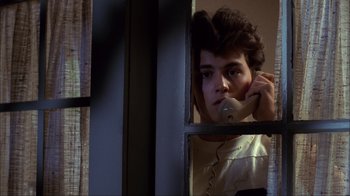 Movie still from “A Nightmare on Elm Street” (1984), directed by Wes Craven – A man holding a phone to his ear while standing in front of a window; Close Up shot, Low angle