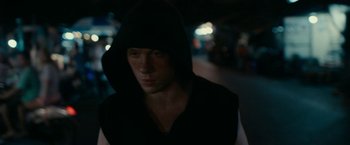 A man in a black hooded sweatshirt is standing in the dark