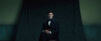 Movie still from “A Quiet Passion” (2016), directed by Terence Davies – A man in a suit and bow tie sitting in a chair; Medium shot, Low angle