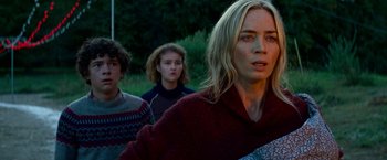 Movie still from “A Quiet Place Part II” (2020), directed by John Krasinski – A group of people standing next to each other in the grass; Medium shot, Low angle
