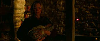 Movie still from “A Quiet Place Part II” (2020), directed by John Krasinski – A woman holding a baby wrapped in a blanket in front of a stone wall; Medium shot, Low angle