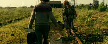 Movie still from “A Quiet Place Part II” (2020), directed by John Krasinski – Two people walking through a field with a bag of food; Medium shot, Low angle