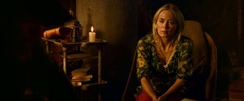 Movie still from “A Quiet Place Part II” (2020), directed by John Krasinski – A woman sitting in front of a lit candle in a dimly - lit room; Medium shot, Over the shoulder angle