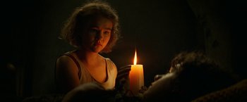 Movie still from “A Quiet Place Part II” (2020), directed by John Krasinski – A young girl holding a lit candle in a dark room; Close Up shot, Over the shoulder angle