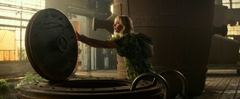 Movie still from “A Quiet Place Part II” (2020), directed by John Krasinski – A woman in a yellow and black dress is touching a large metal object; Wide shot, Low angle