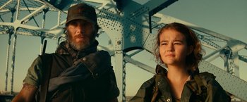 Movie still from “A Quiet Place Part II” (2020), directed by John Krasinski – A man and a woman standing next to each other in front of a bridge; Close Up shot, Low angle