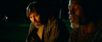 Movie still from “A Quiet Place Part II” (2020), directed by John Krasinski – A man with long hair and a beard wearing a plaid shirt; Close Up shot, Over the shoulder angle